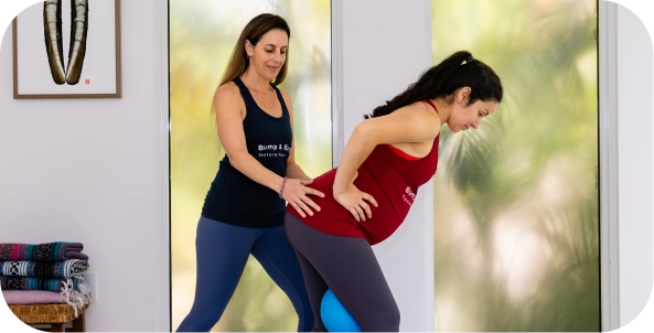 An instructor supporting a pregnant client in a standing lunge stretch