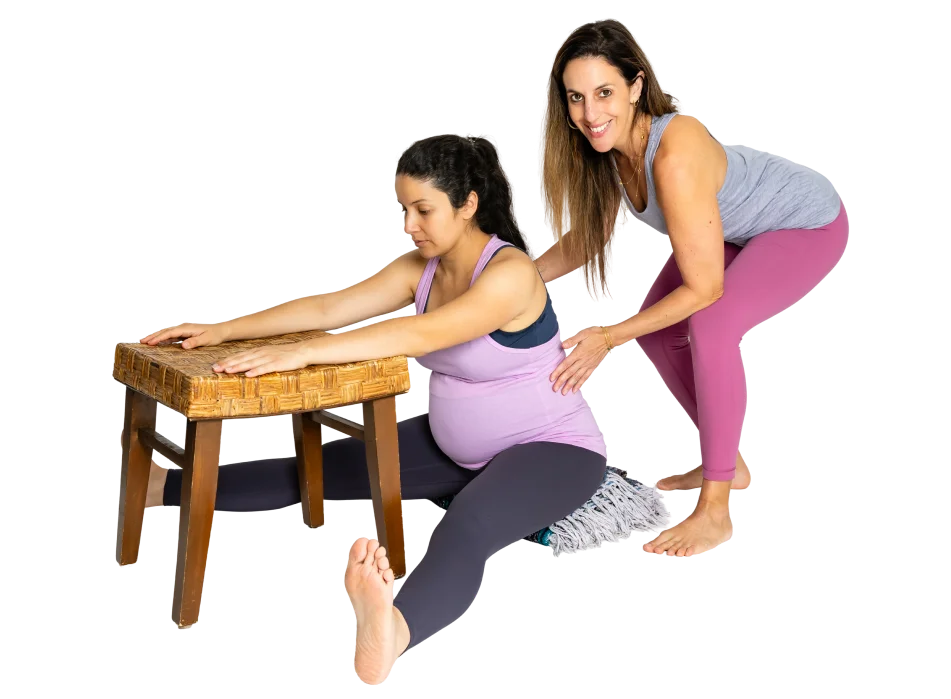 An instructor guiding a pregnant client through a supported forward fold over a stool