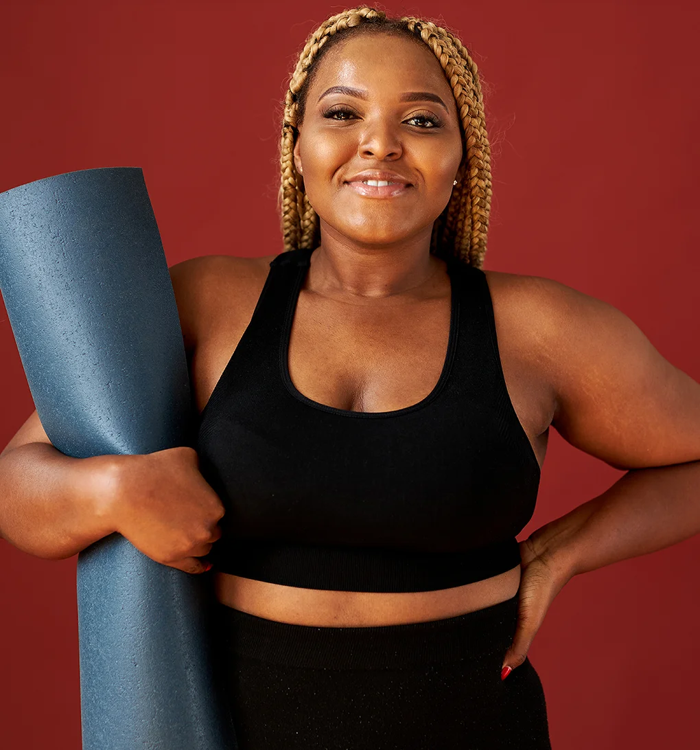 A smiling woman stretching her arms overhead while seated on an exercise ball