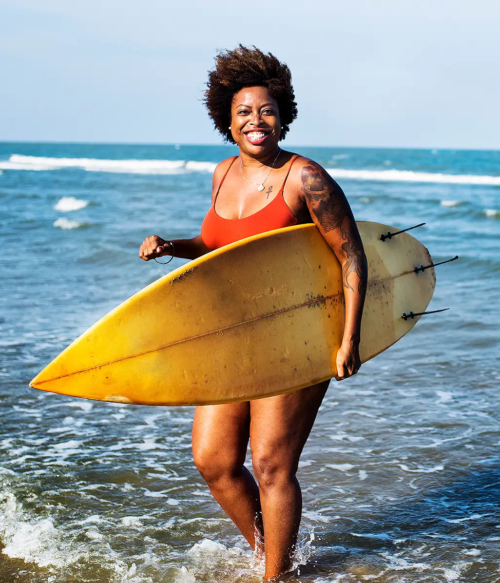 A smiling woman carrying a surfboard out of the sea